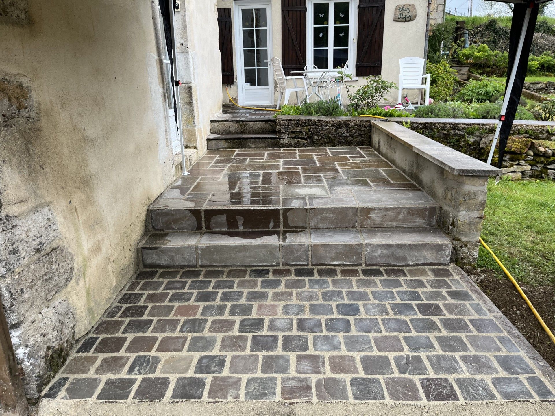 Des marches en pierre et un chemin pavé mènent à l'entrée d'une maison avec des portes et des fenêtres blanches.