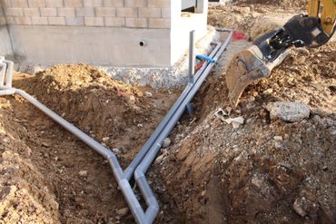 Tranchée de construction avec des tuyaux en PVC gris menant aux fondations d'une maison.