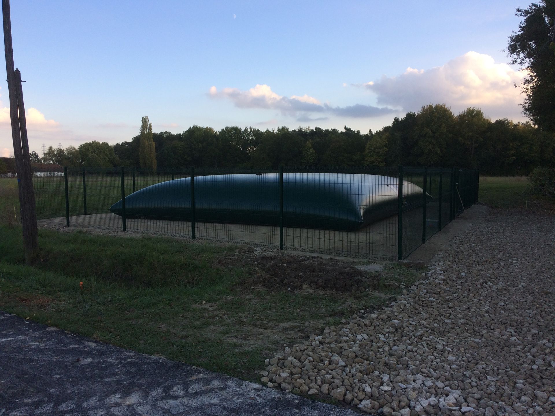 Piscine rectangulaire couverte, entourée d'une clôture noire, dans une cour extérieure gazonnée.