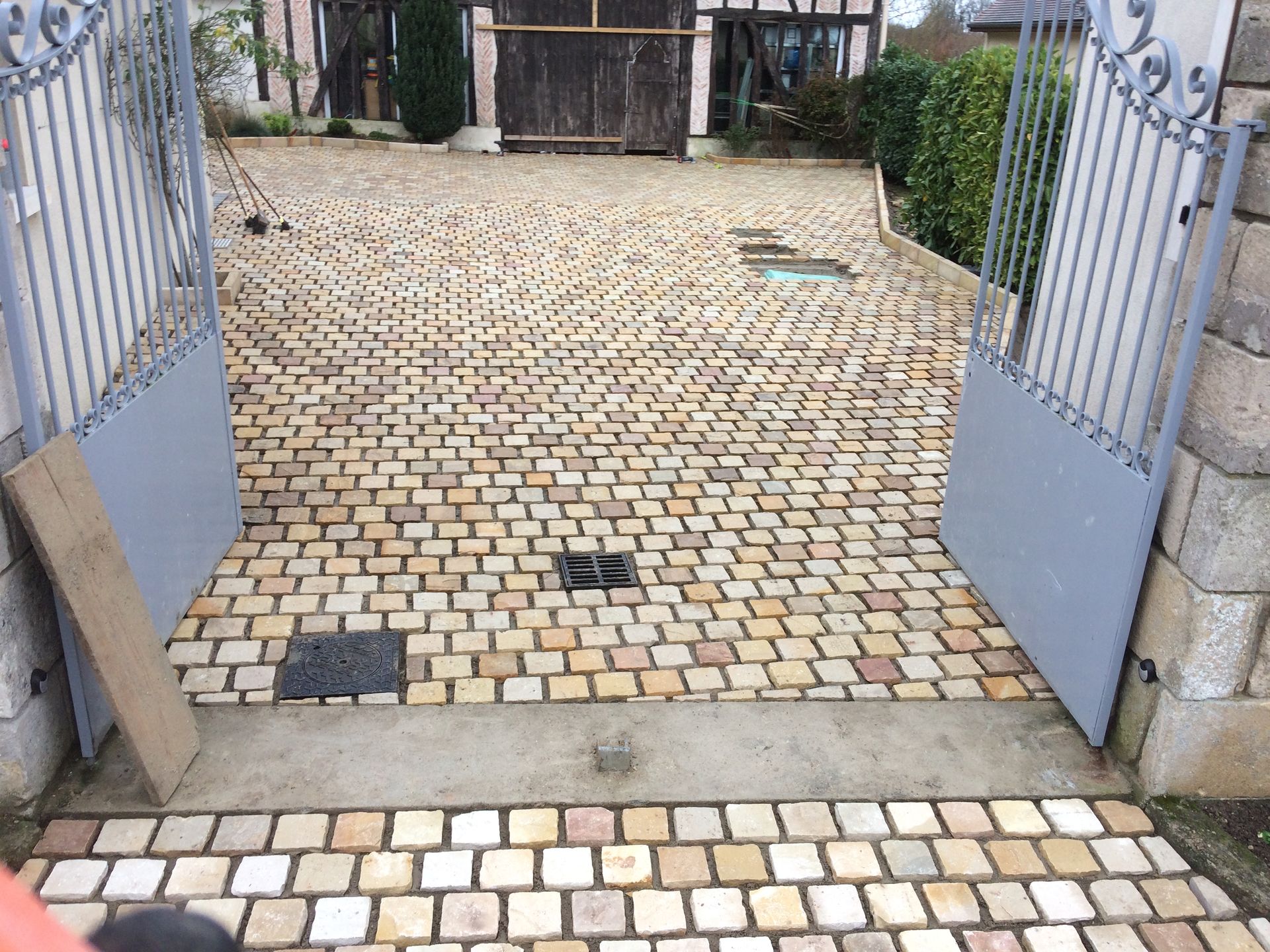 Portail métallique ouvert donnant sur une cour pavée.