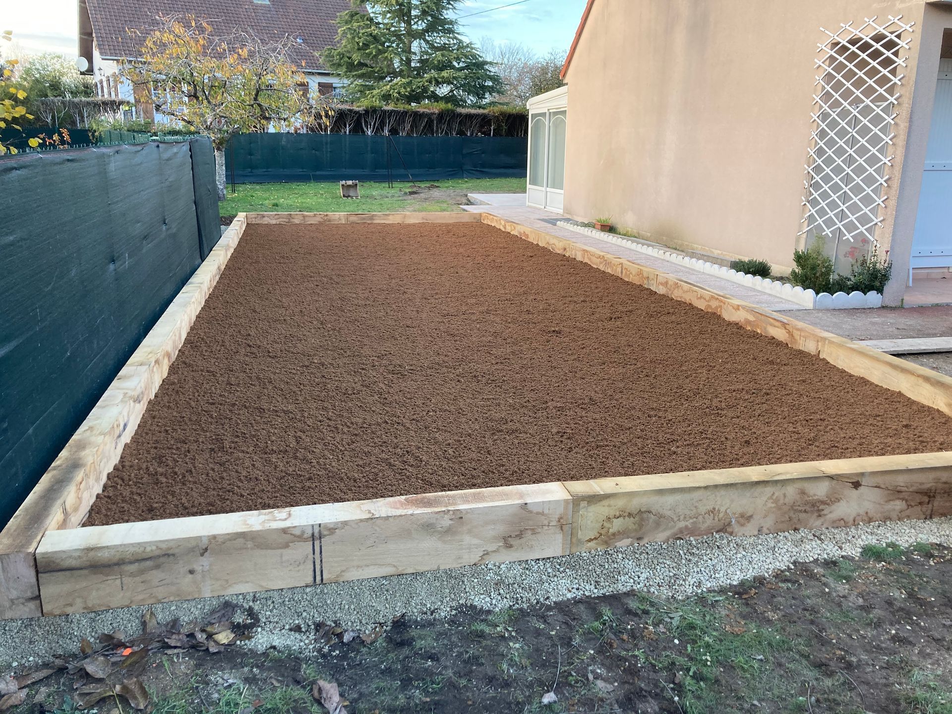 Cour arrière fraîchement aménagée avec un parterre rectangulaire bordé de pierres et d'un mur de maison.