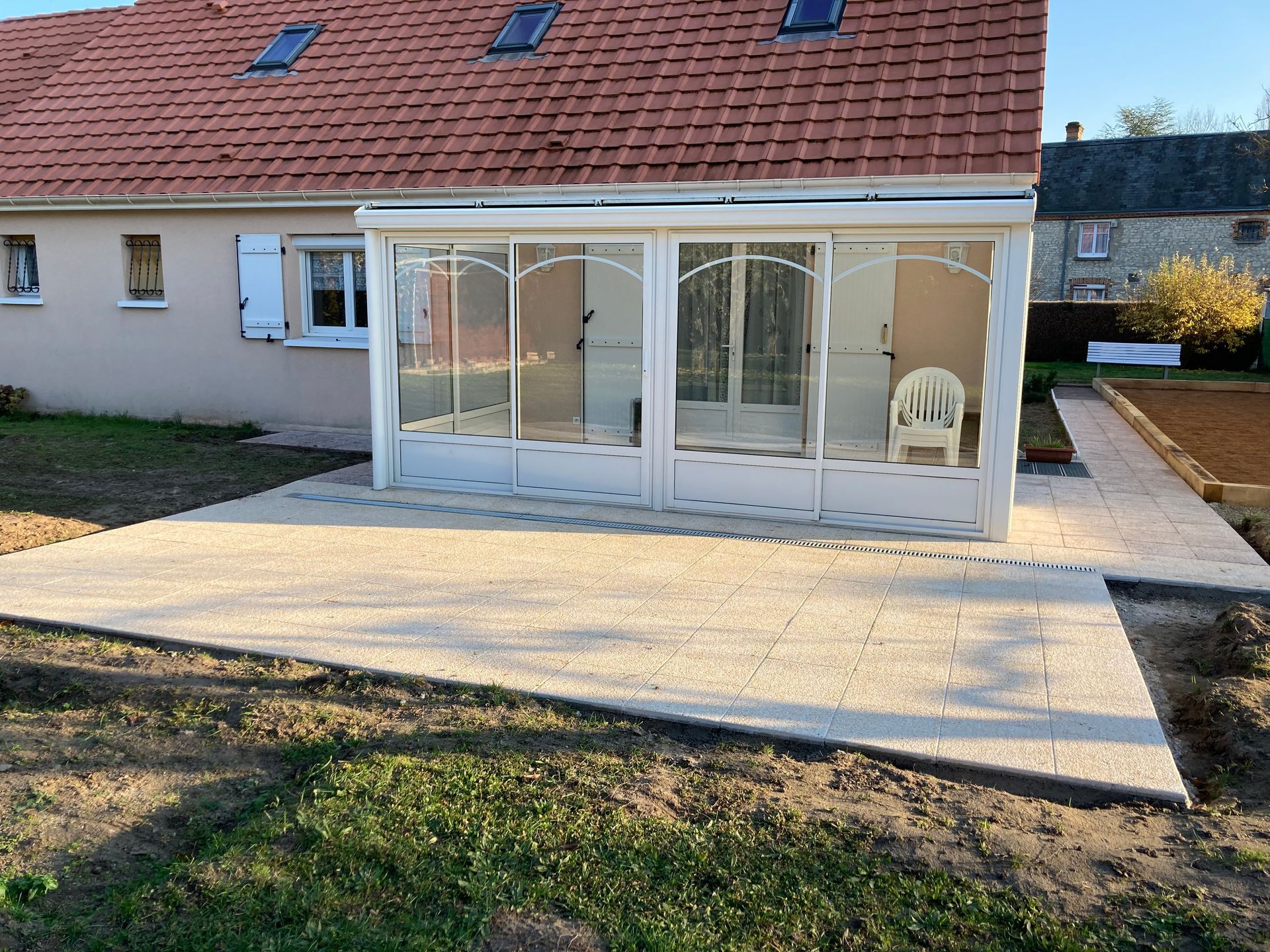 Terrasse couverte avec de grandes portes vitrées attenantes à une maison, jouxtant une allée pavée et une pelouse.