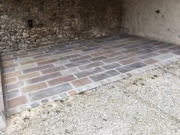 Terrasse en pierre nue avec pavés de brique, jouxtant une zone de gravier et un mur en pierre.