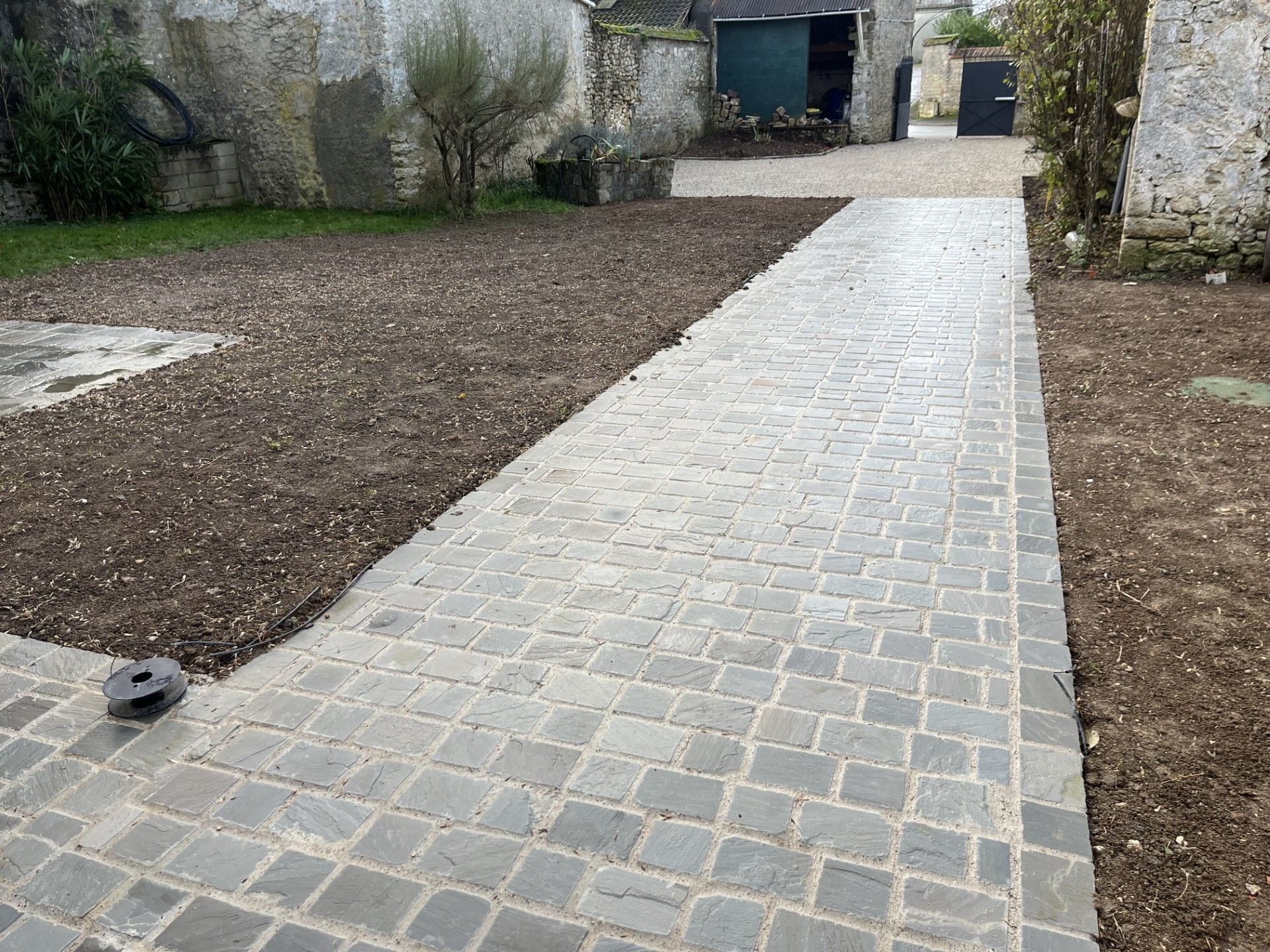 Chemin pavé traversant une cour intérieure et menant à une porte, bordé de part et d'autre par un sol.