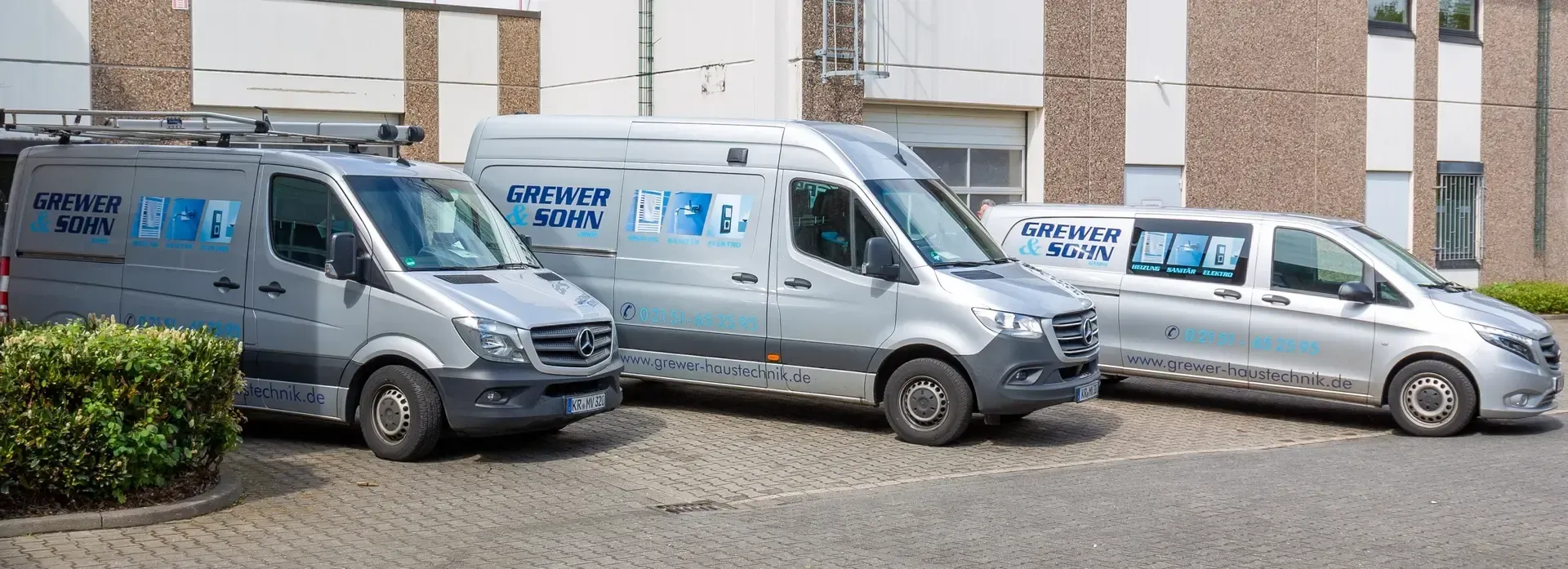 Auf einem Parkplatz vor einem Gebäude stehen drei Lieferwagen.