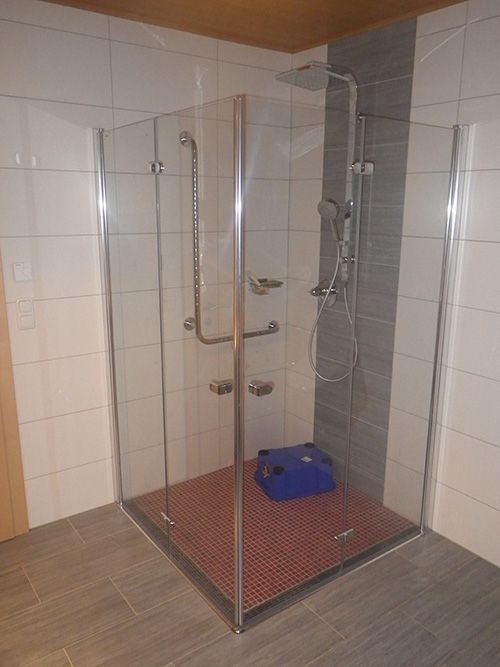 Ein Badezimmer mit ebenerdiger Dusche und einem blauen Eimer auf dem Boden.