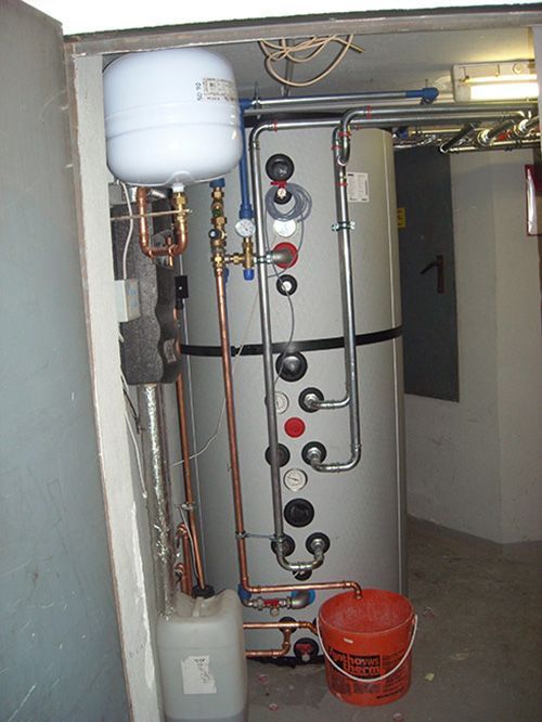 Ein großer Grauwassertank mit Kupferrohren und einem Eimer daneben