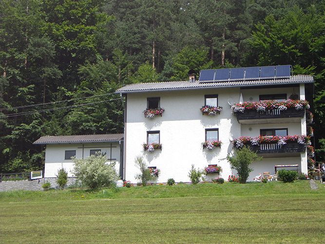 Ein weißes Haus mit Blumen auf den Balkonen und Sonnenkollektoren auf dem Dach