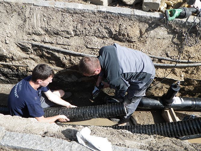 Zwei Männer arbeiten an einem Rohr im Dreck