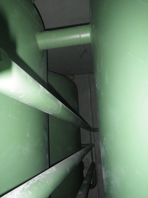 Neben einer Wand in einem Raum steht eine grüne Mülltonne.