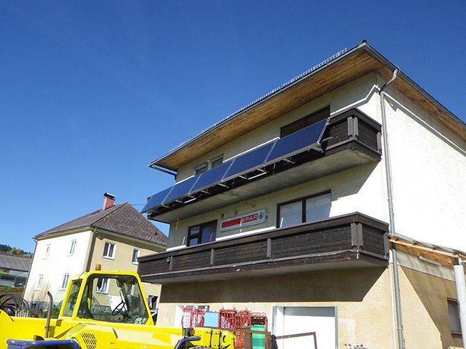 Ein gelber Lastwagen parkt vor einem Gebäude mit Solarmodulen auf dem Dach.
