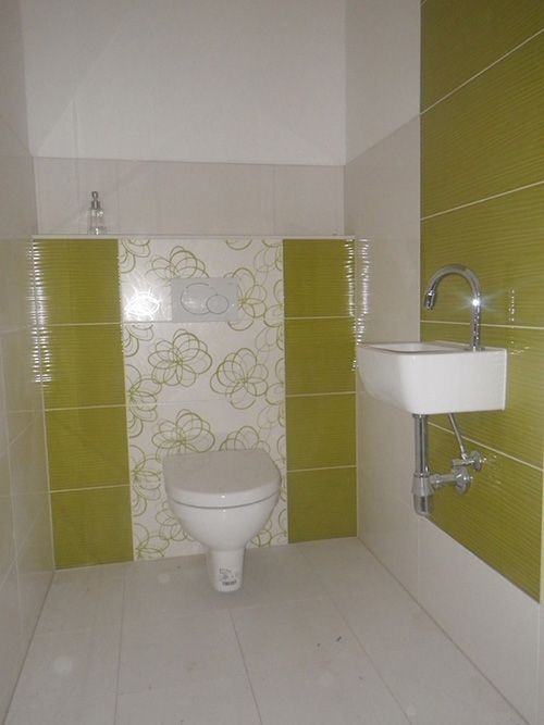 Ein Badezimmer mit Toilette, Waschbecken und grünen Fliesen.