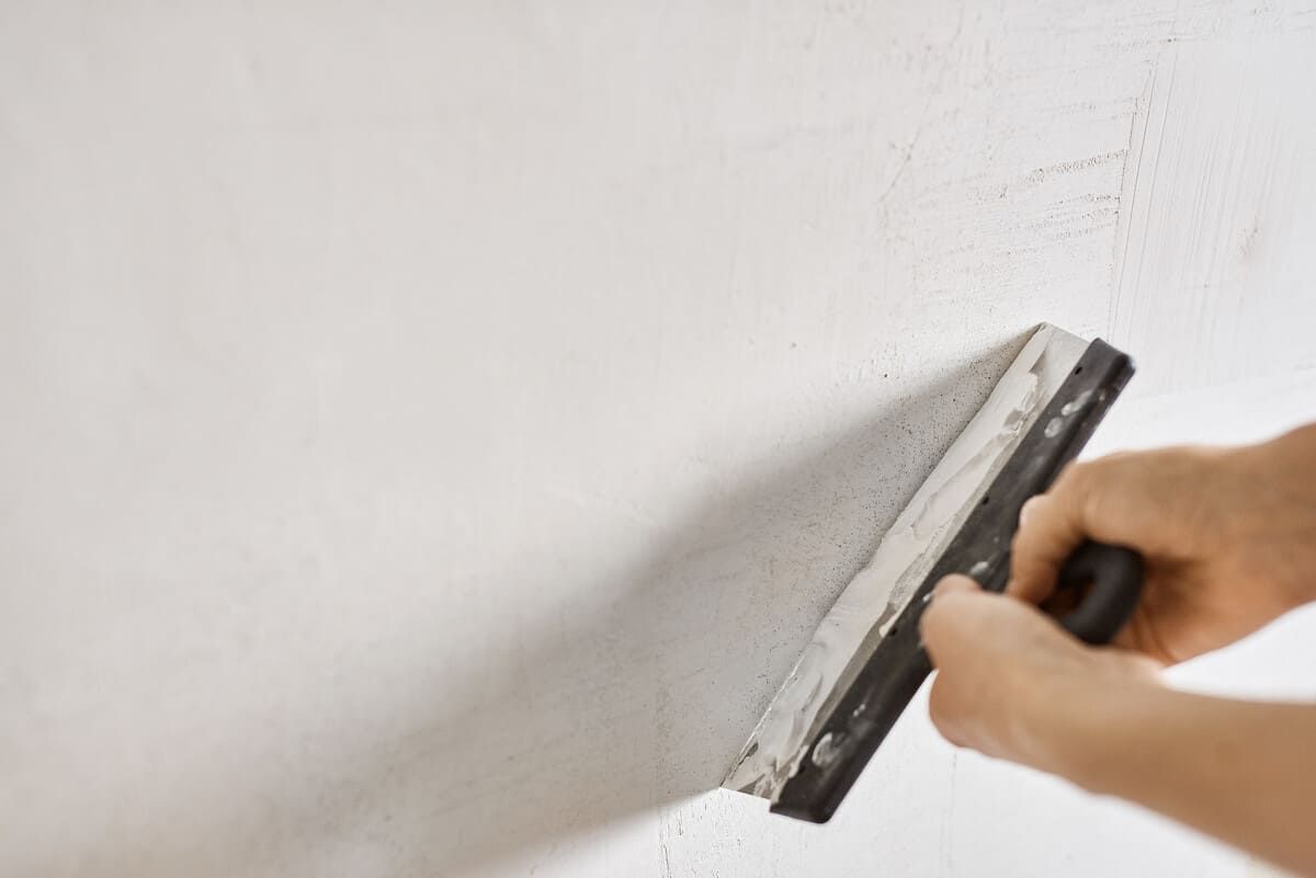 Manos utilizando una espátula para alisar yeso blanco en una pared.