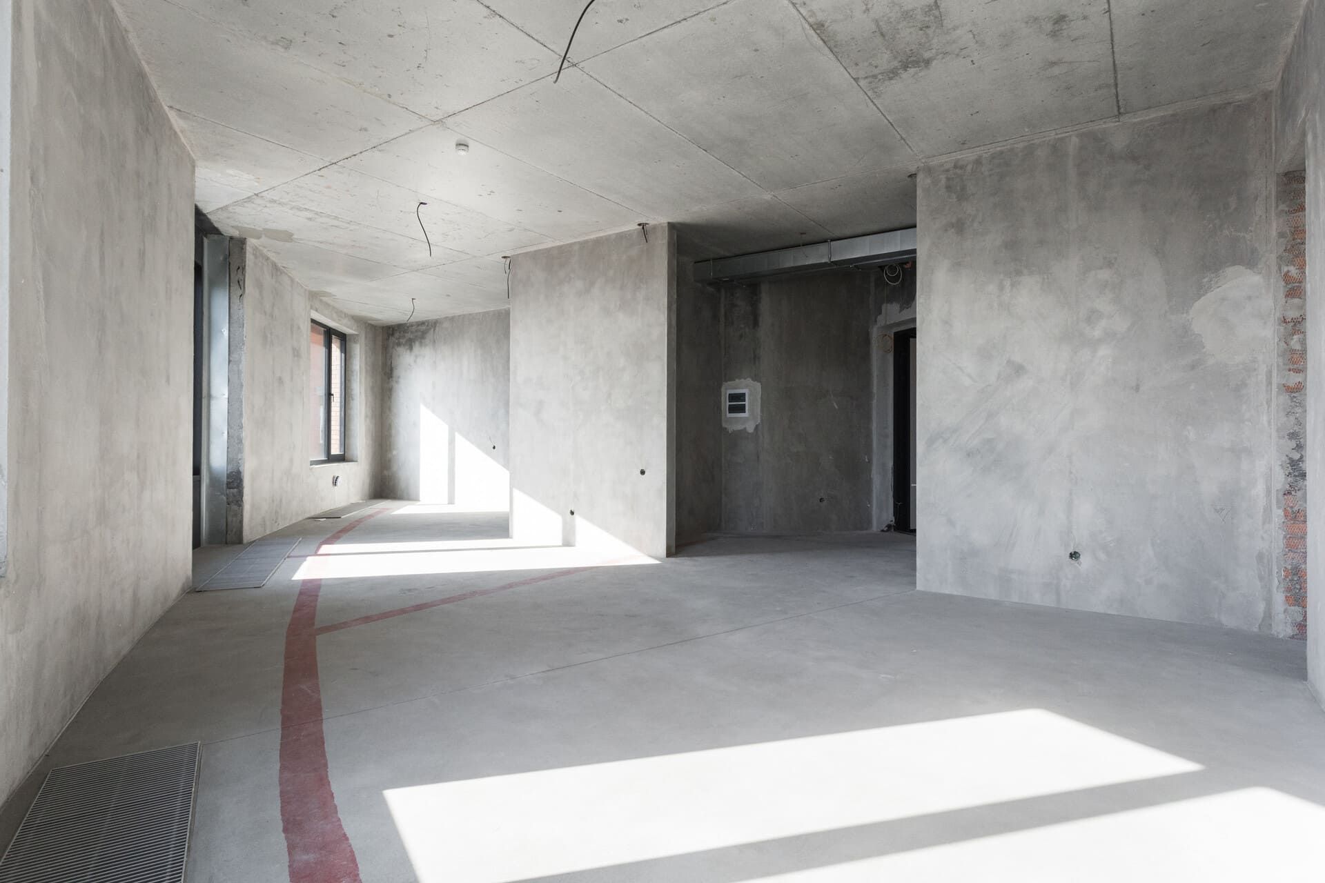 Interior de un edificio de hormigón en construcción, con la luz del sol entrando a través de las ventanas, resaltando las paredes y pisos sin terminar.
