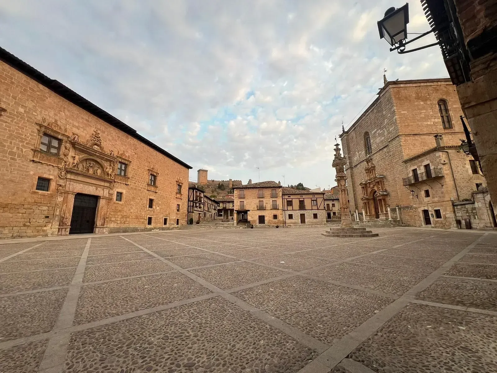 Plaza vacía de adoquines enmarcada por antiguos edificios de piedra bajo un cielo nublado.