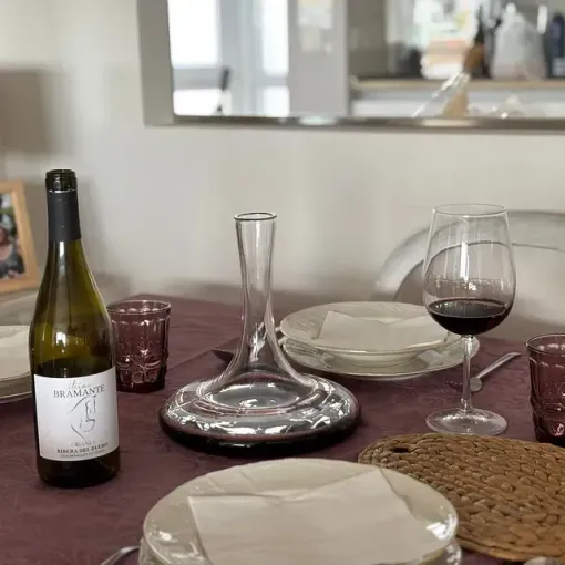 Botella y copa de vino sobre una mesa puesta con platos, decantador y un camino de mesa color burdeos.