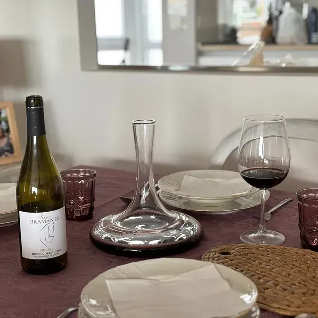 Botella y copa de vino sobre una mesa puesta con platos, decantador y un camino de mesa color burdeos.
