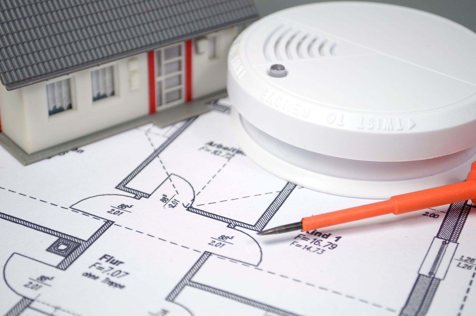 Miniaturhaus, Rauchmelder, Schraubenzieher und Bauplan.