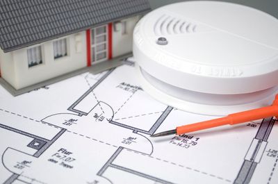 Miniaturhaus, Rauchmelder, Schraubenzieher und Bauplan.