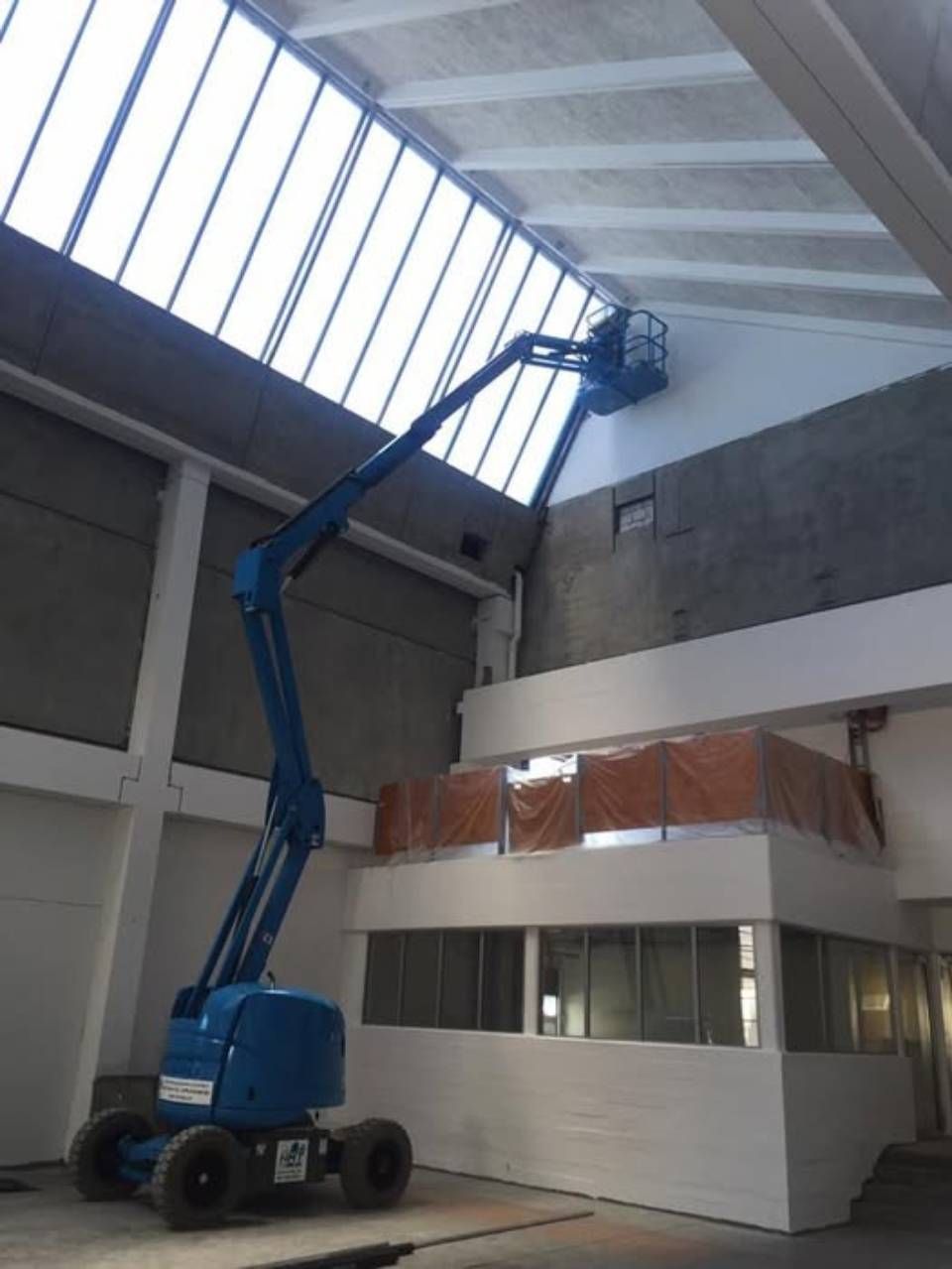 Eine blaue Hubarbeitsbühne, die bis zu einem Oberlicht in einem Industriegebäude reicht.