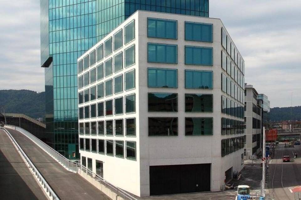 Ein modernes, weißes Glasgebäude steht neben einem hohen, türkisfarbenen Glasgebäude.