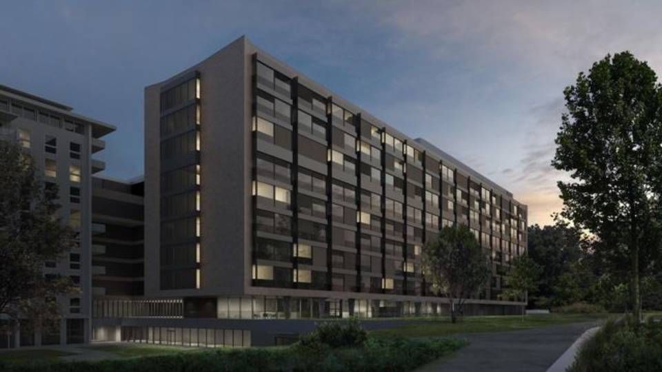 Modernes graues Wohnhaus in der Abenddämmerung, mit vielen Fenstern, neben einer Rasenfläche und Bäumen.