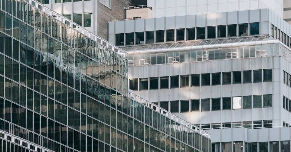 Glas- und graue Bürogebäude im urbanen Umfeld, die Sonnenlicht und einander reflektieren.
