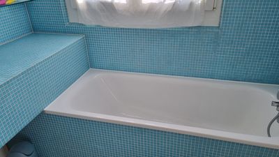 Duschwand mit einer fehlenden Fliese, die den Betonuntergrund freilegt. Beige Fliesen.