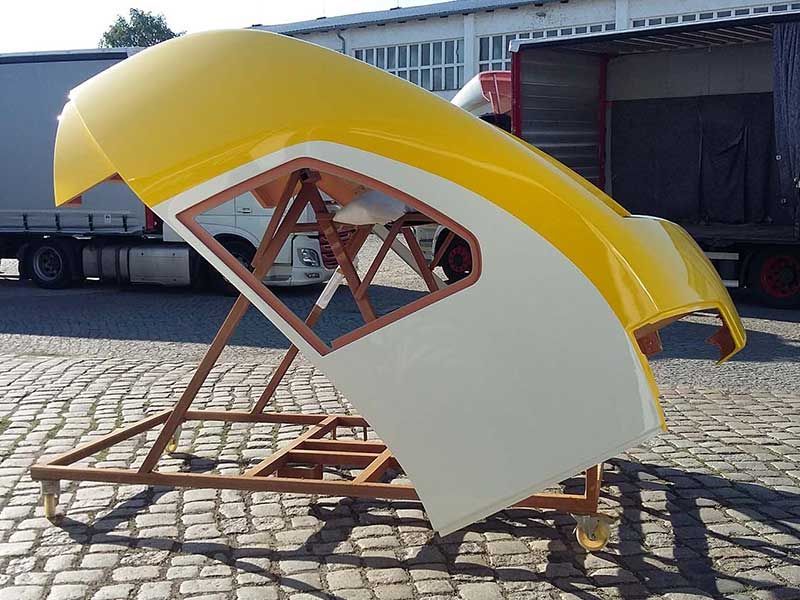 Gelb-weiße Karosserieteile auf einem braunen Metallständer im Freien. 