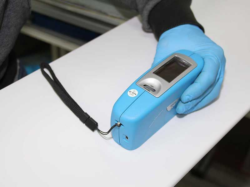 Eine Person mit blauen Handschuhen hält ein hellblaues Handmessgerät mit Bildschirm