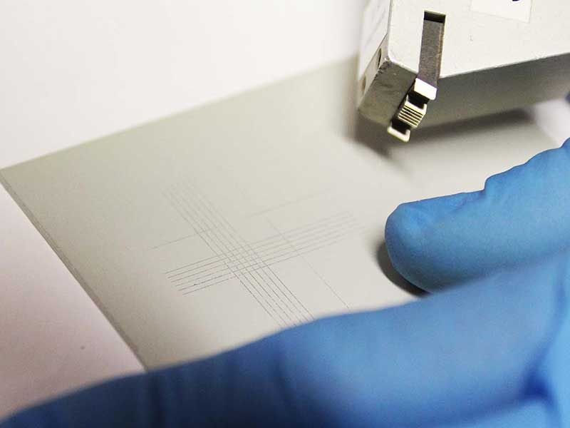 Eine behandschuhte Hand hält eine graue Oberfläche mit feinen Linien. 