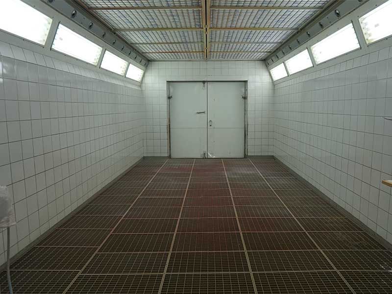 Leere, weiß geflieste Spritzkabine mit Metallbodengittern