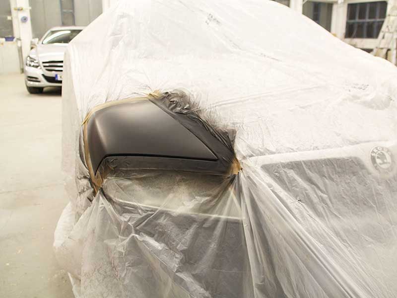 In einer Reparaturwerkstatt wird der Seitenspiegel eines Autos schwarz lackiert
