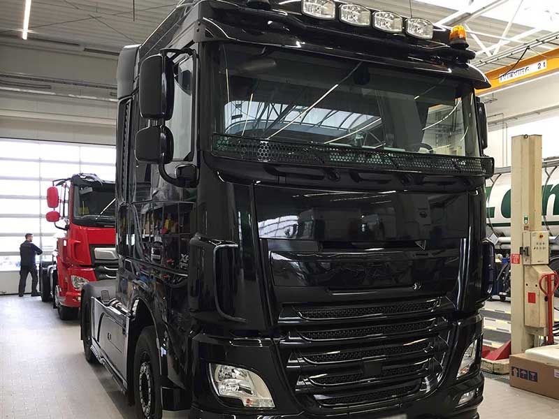 Schwarzer DAF-LKW in einer Fabrikanlage, roter LKW dahinter.