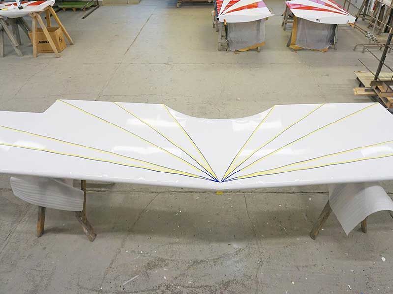 Weißer Flugzeugflügel mit gelben Streifen in einer Werkstatt.