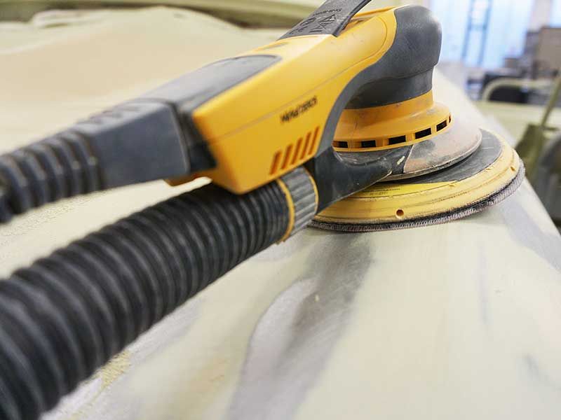 Gelber Exzenterschleifer beim Schleifen der Fahrzeugoberfläche