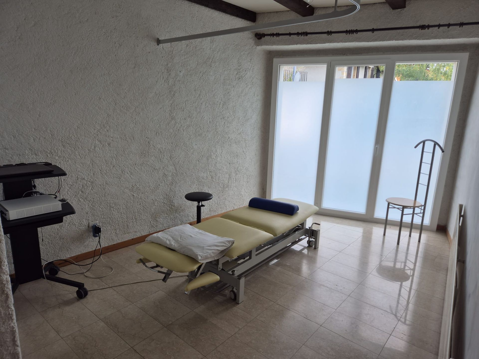 Une salle de soins avec table de massage, murs en bois, petite étagère avec fournitures et une chaise.