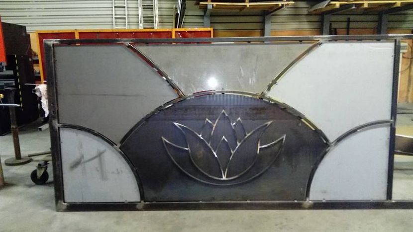 Un panneau de portail métallique en cours de fabrication, présentant un motif de lotus central découpé au laser et encadré par des segments d'acier incurvés.