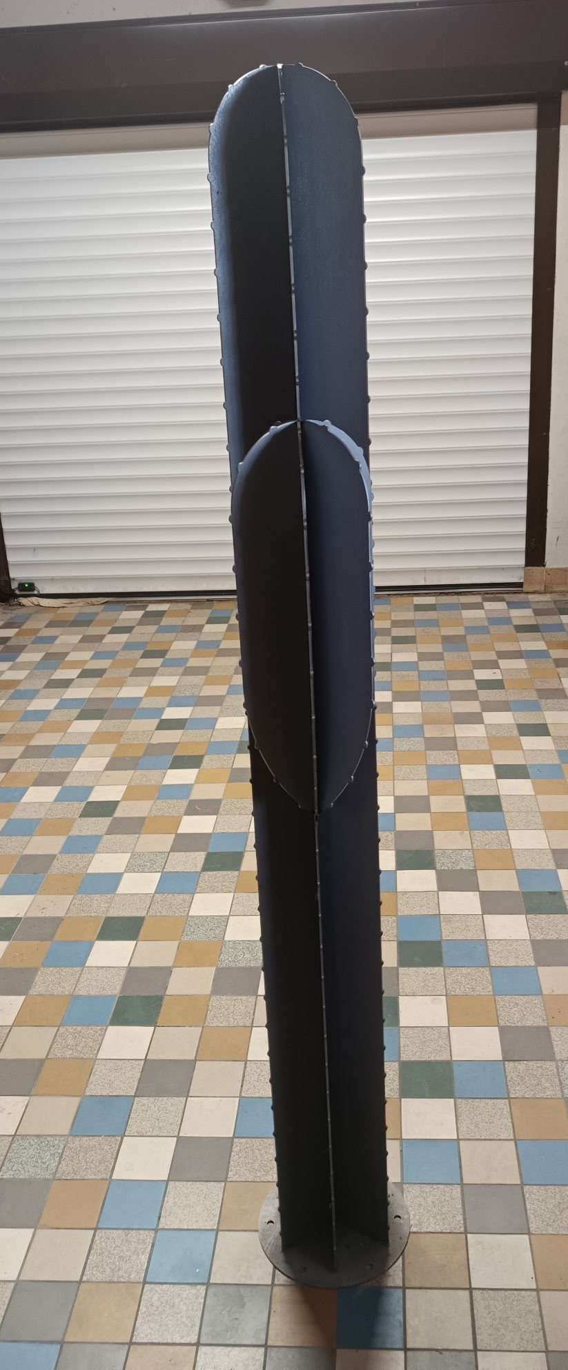 Un grand panneau acoustique vertical gris foncé à ailettes multiples, posé sur un sol carrelé à damier dans une grande pièce.