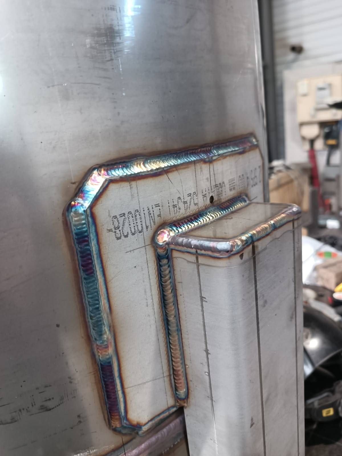 Soudures en acier inoxydable propres fixant une plaque métallique rectangulaire et un tube à un grand réservoir cylindrique.