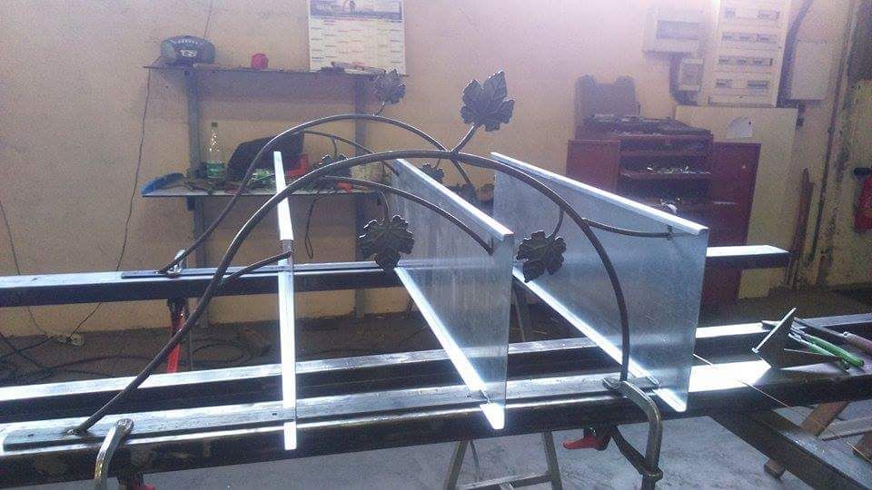 Rambardes métalliques cintrées ornées de motifs de feuilles, fixées à un établi dans un atelier.