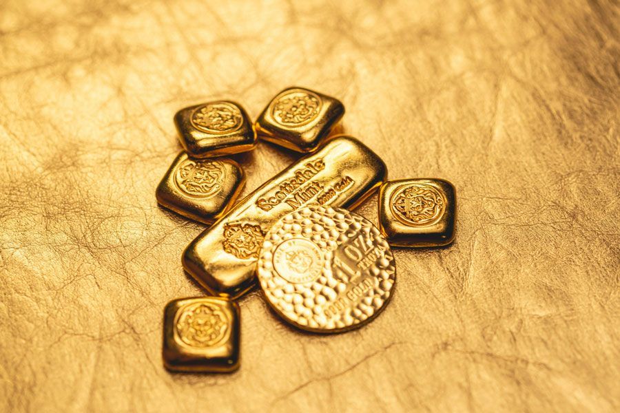 Mehrere kleine Goldbarren und eine Anlagemünze auf goldenem Hintergrund, Symbolbild für Anlagegold, Edelmetallhandel sowie den Verkauf von Goldbarren und Goldmünzen beim Goldankauf in Hamburg.