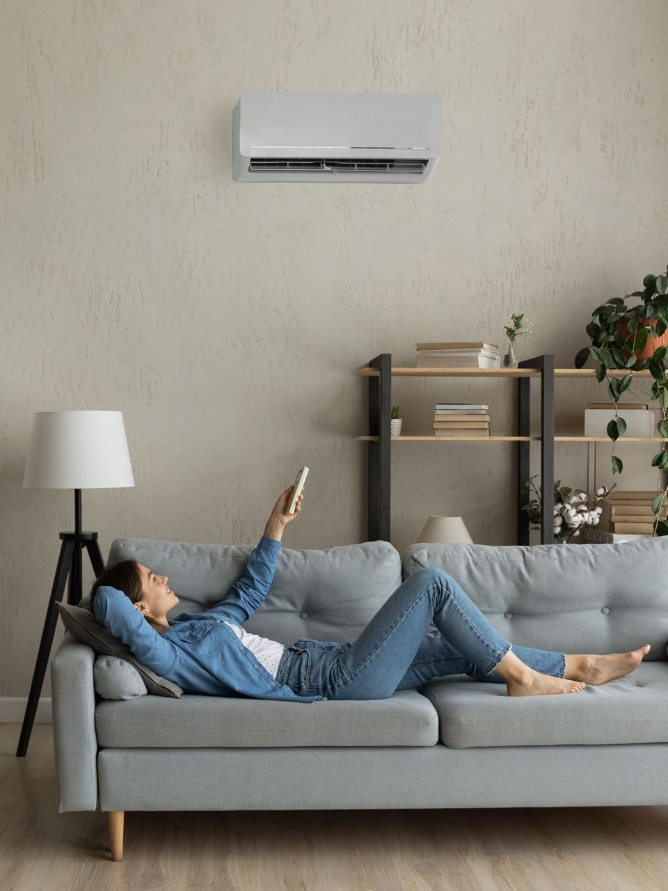 Jeune femme sur un canapé, allumant la climatisation avec une télécommande