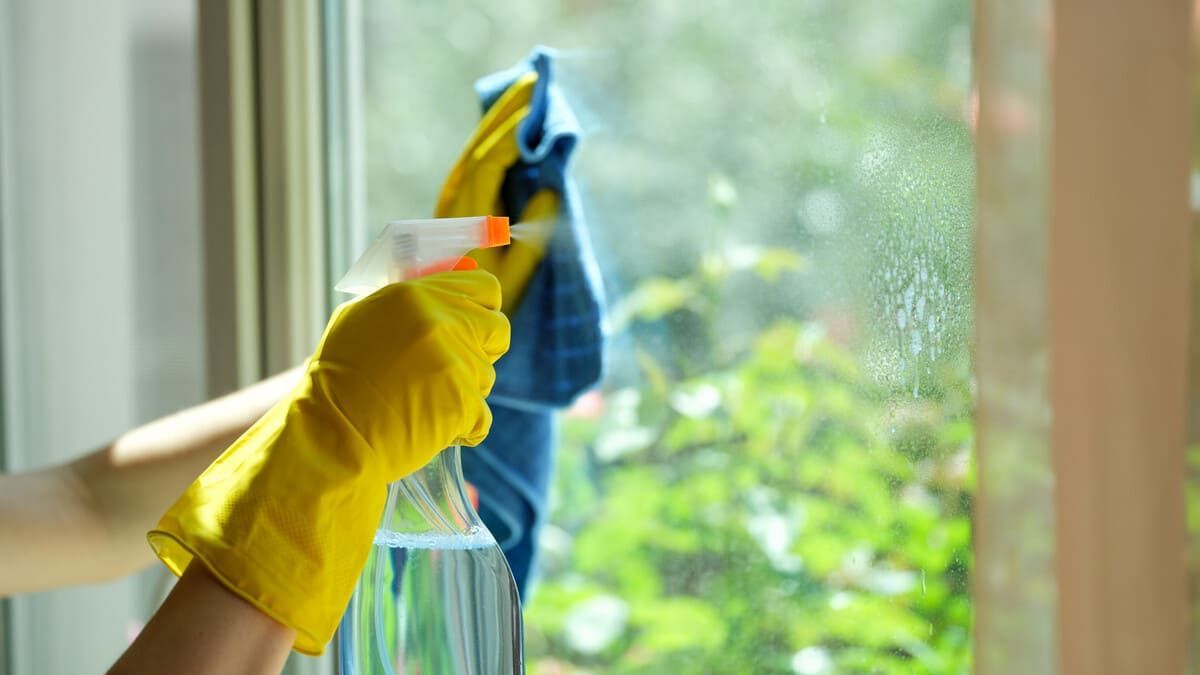 Una persona está limpiando una ventana con una botella de spray y un paño.