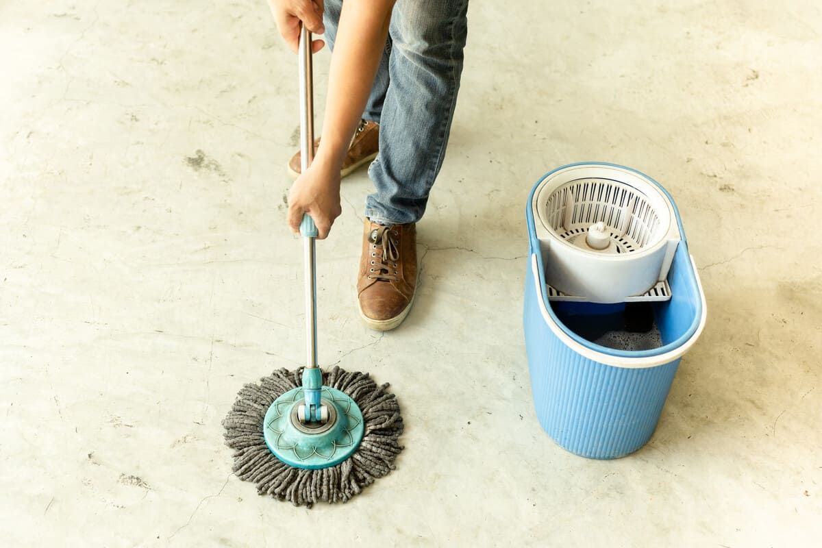Una persona está limpiando el piso con un trapeador y un balde.