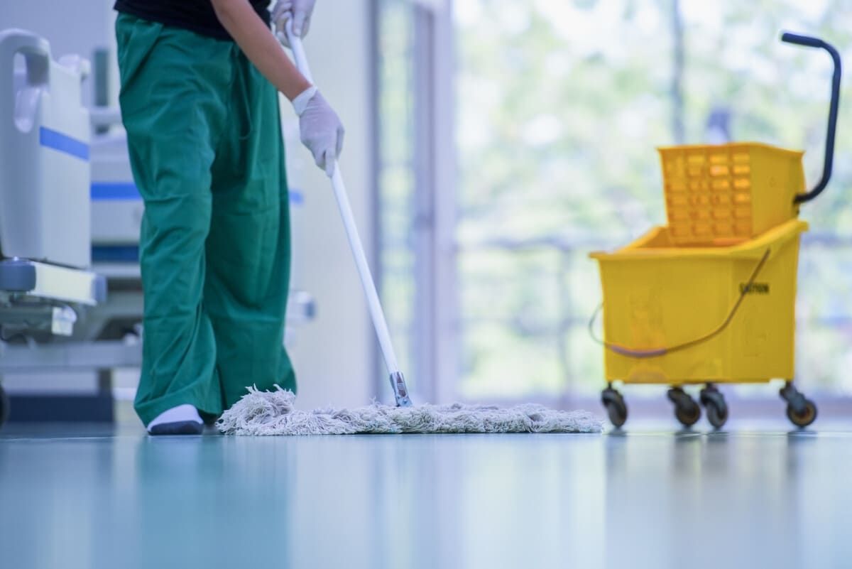 Una persona está fregando el suelo de un hospital con un trapeador.