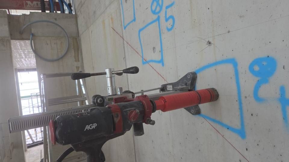 Eine rot-schwarze Bohrmaschine ist durch eine Wandöffnung im Inneren einer Baustelle montiert.