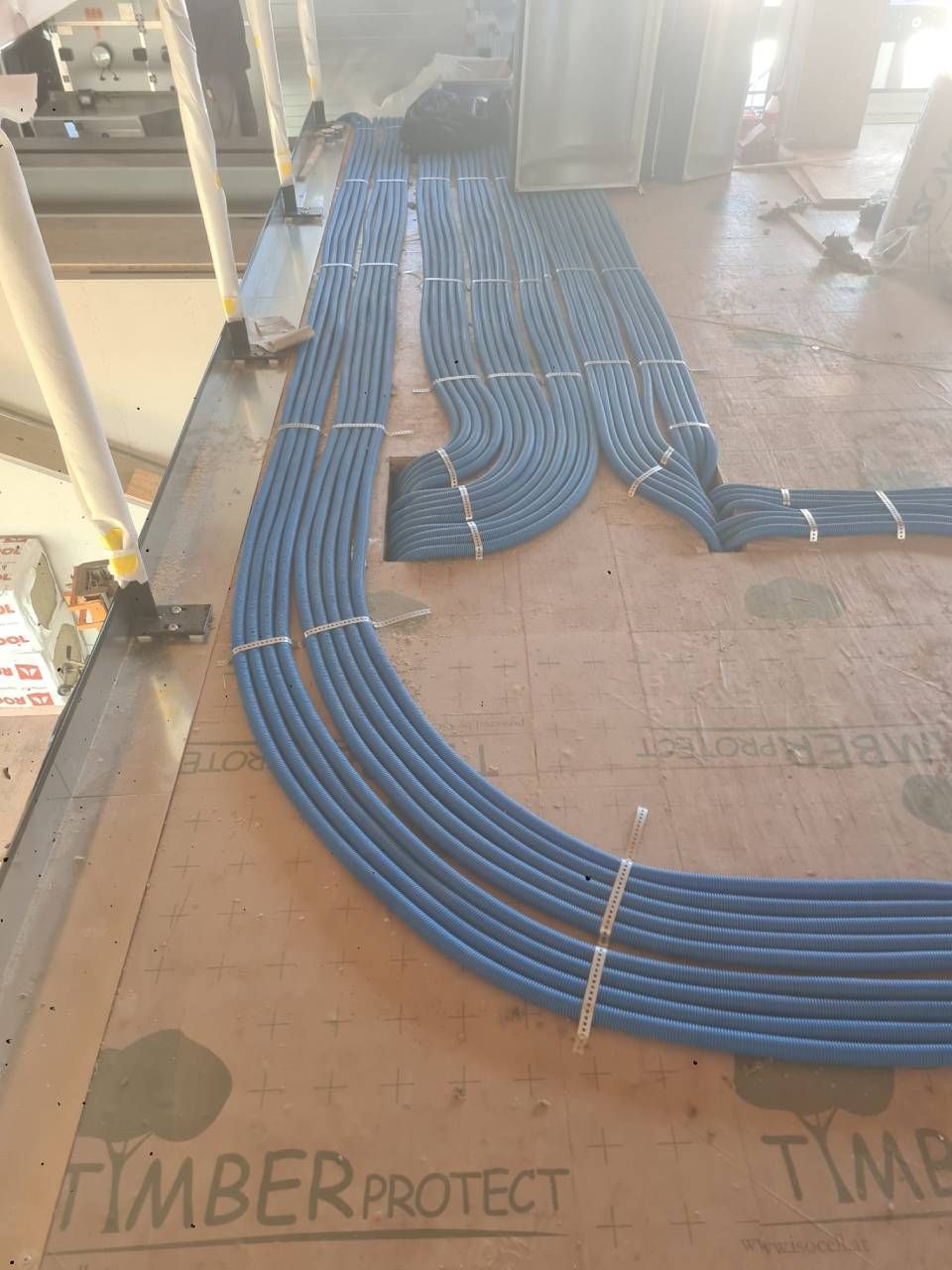 Blaue Elektrokabel, ordentlich gebündelt über einen im Bau befindlichen Boden verlegt.