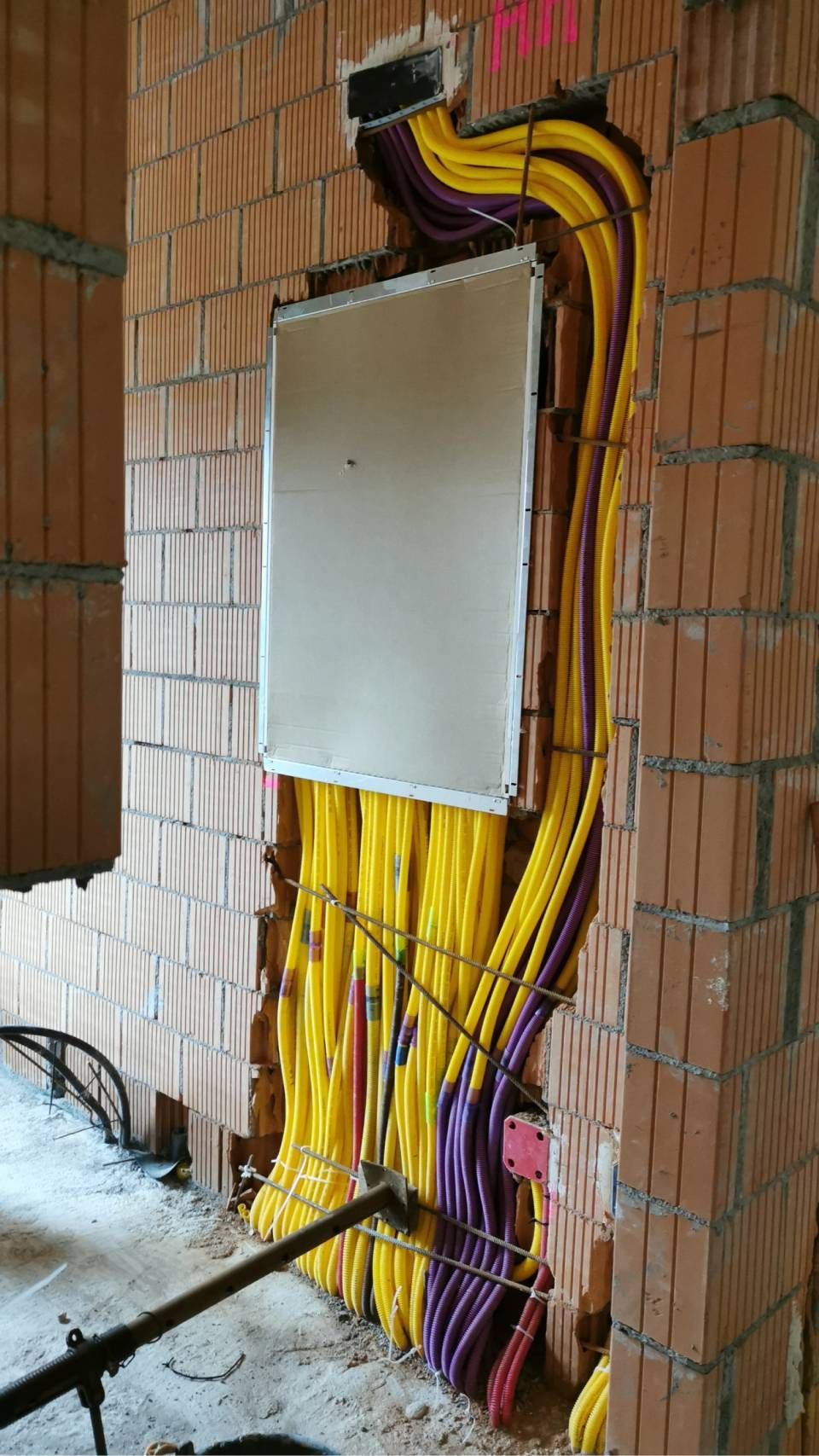 Elektrischer Verteilerkasten mit freiliegenden gelben und violetten Drähten, montiert an einer Ziegelwand im Inneren eines Gebäudes.