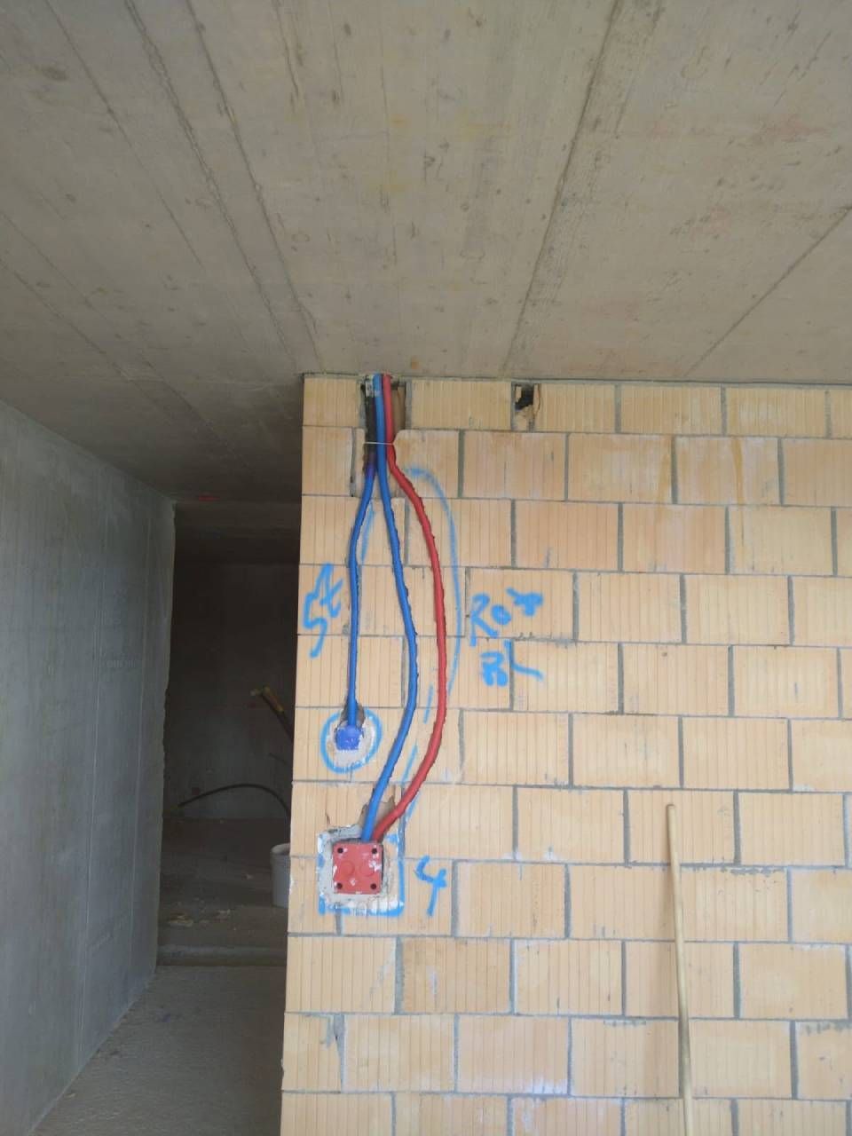 Freiliegende rote und blaue Kabel und Steckdosen an einer gefliesten Wand unter einer Betondecke in einem unfertigen Raum